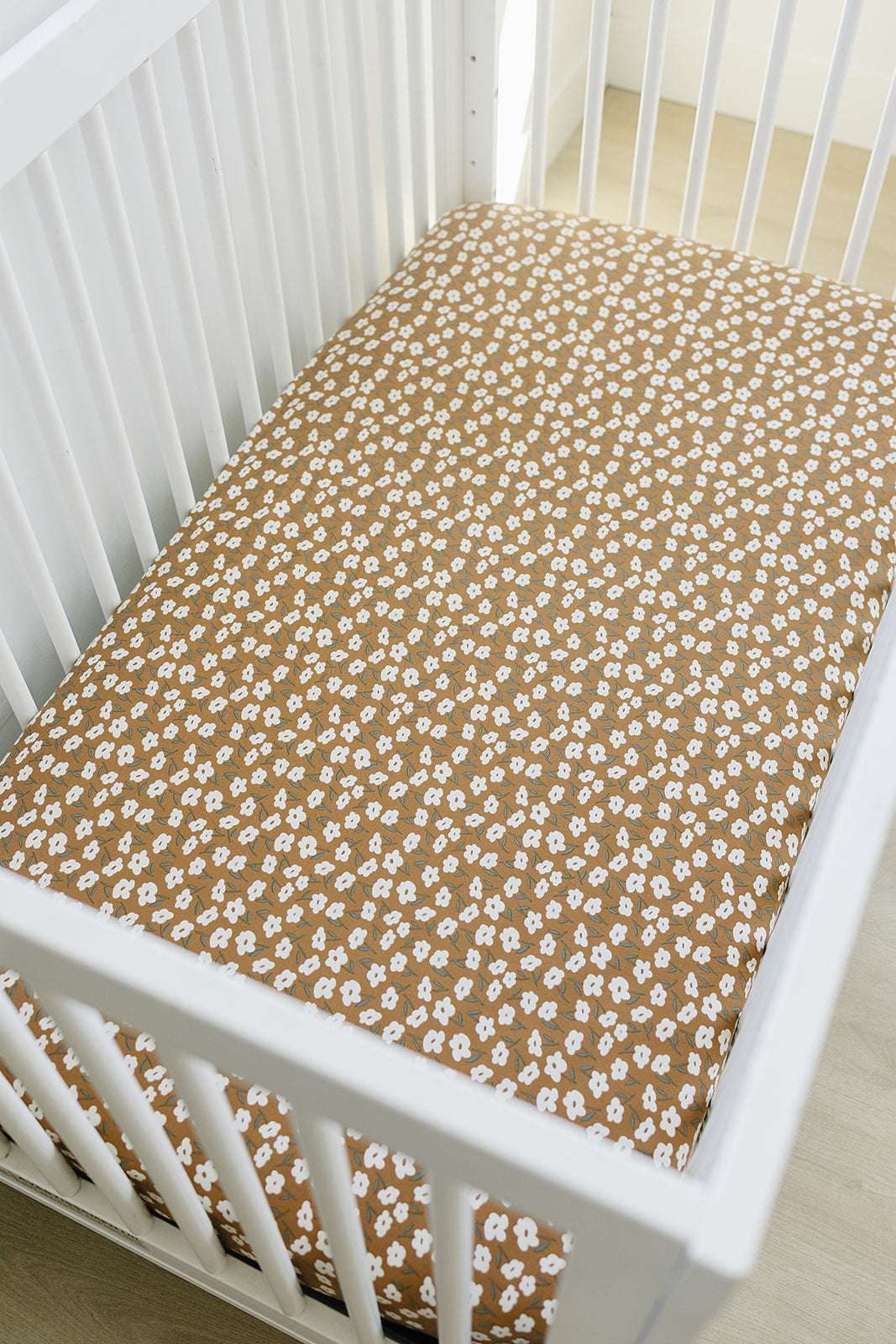 Bamboo Stretch Crib Sheet - Mustard Floral in a cozy crib, featuring a vibrant floral pattern on a warm mustard background.