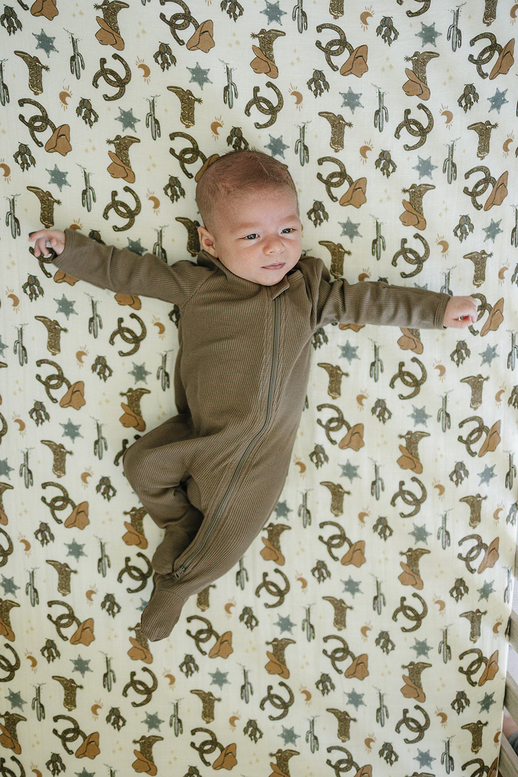 Baby lying on a muslin crib sheet featuring an Outlaw Cowboy print, highlighting comfort and style.