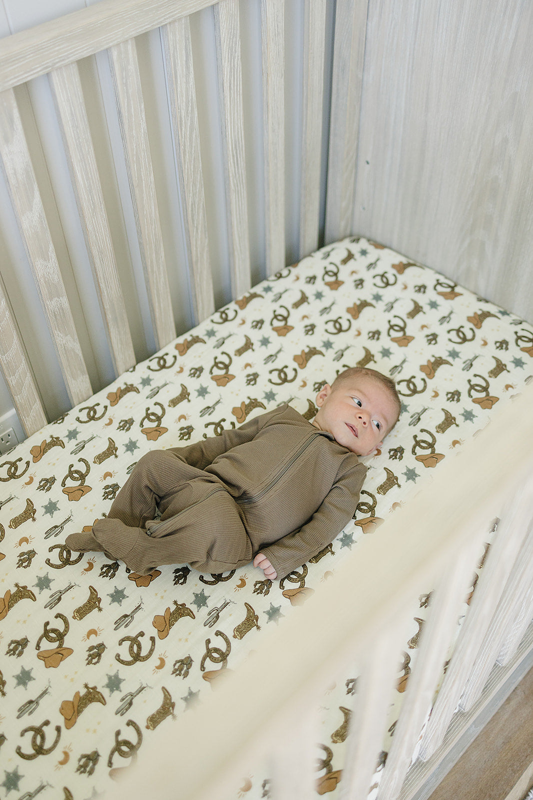 Baby lying on Muslin Crib Sheet - Outlaw Cowboy featuring playful cowboy elements.