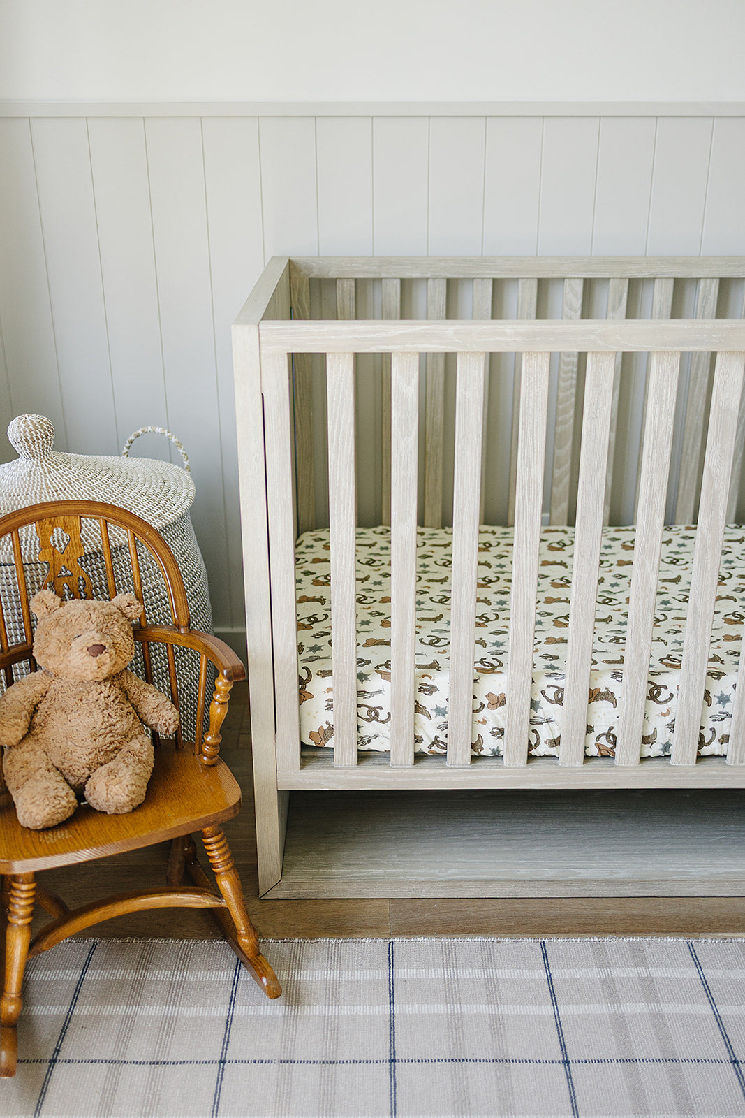 Muslin crib sheet in crib with wooden rocking chair and teddy bear in nursery with western theme.