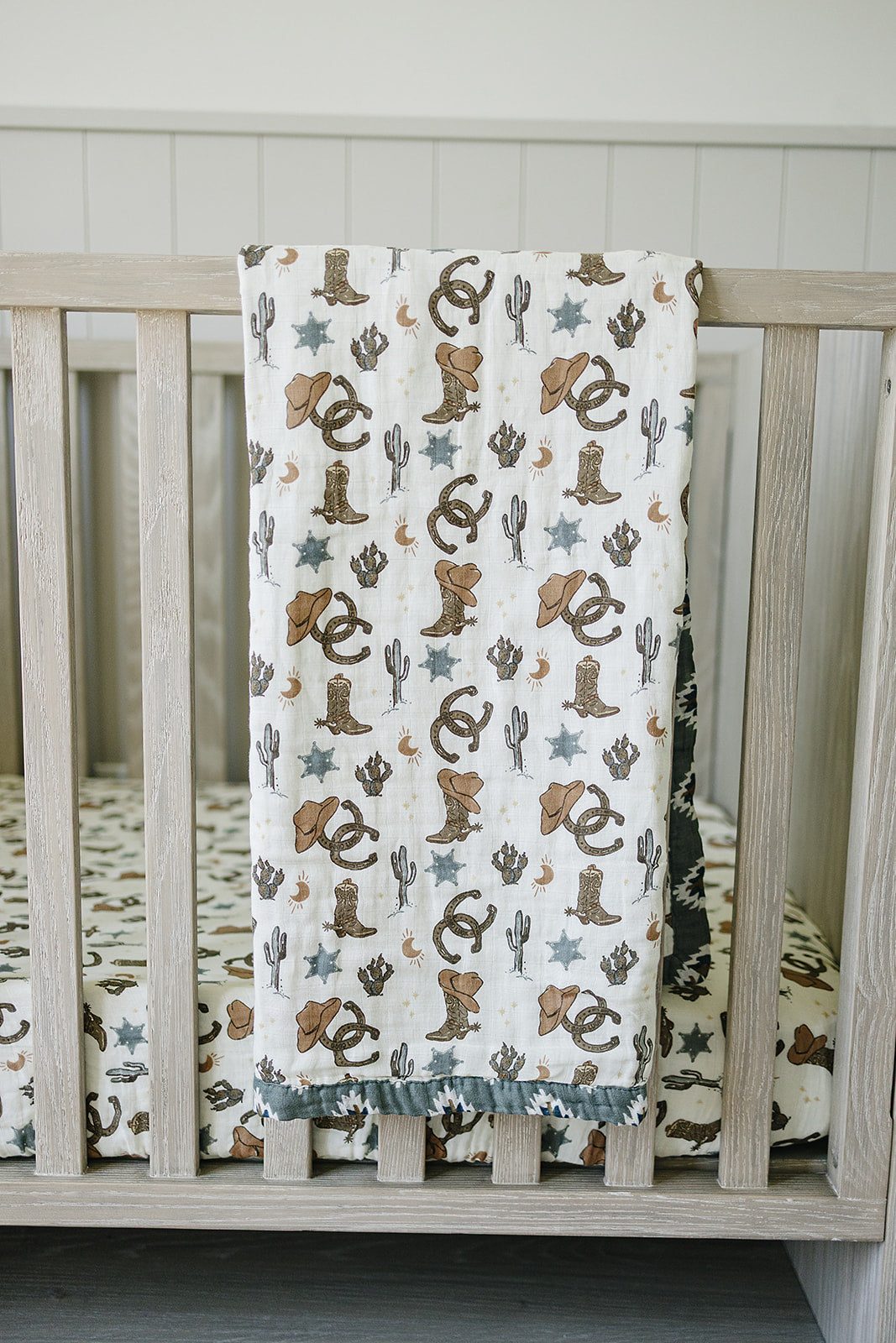 Muslin crib sheet Outlaw Cowboy with playful western designs featuring cowboy hats and cacti in a nursery setting.