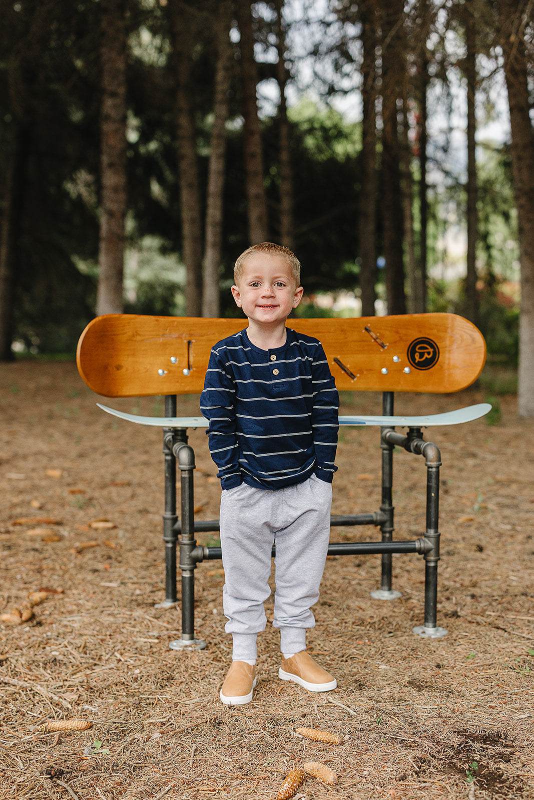 Smiling child wearing a navy stripe long sleeve tee for kids, standing in front of a wooden skateboard bench outdoors.