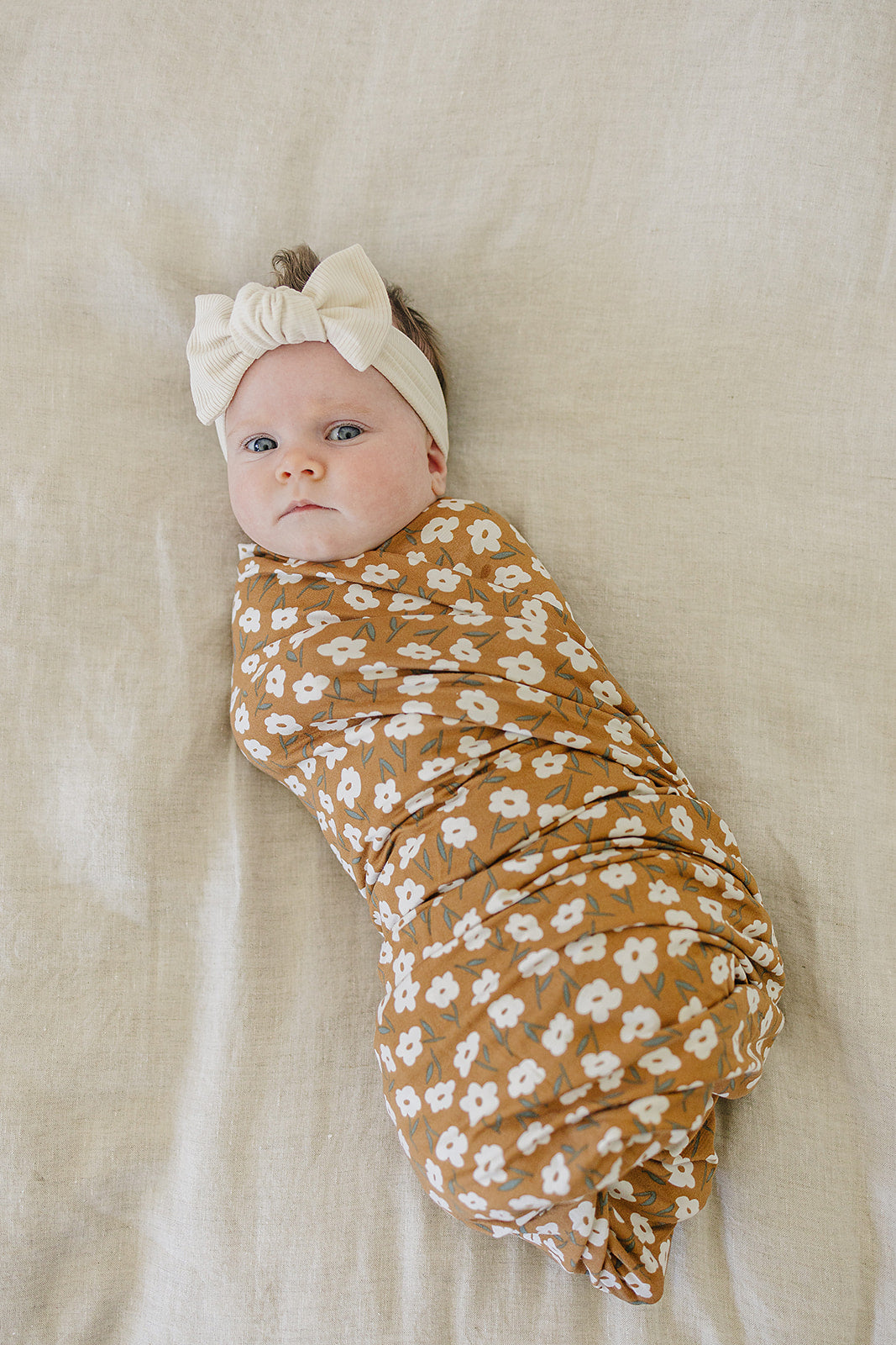 Bamboo Stretch Swaddle Mustard Floral - Baby wrapped in floral swaddle on neutral backdrop, showcasing comfort and style.