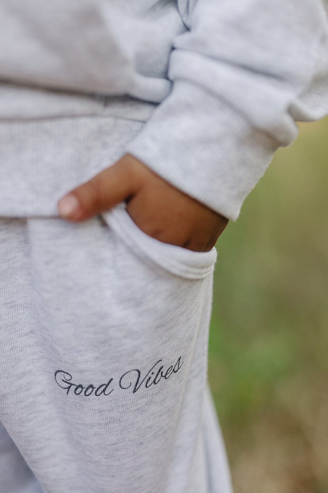 Close-up of a child's hand in pocket of Good Vibes unisex french terry school outfit in neutral tones.
