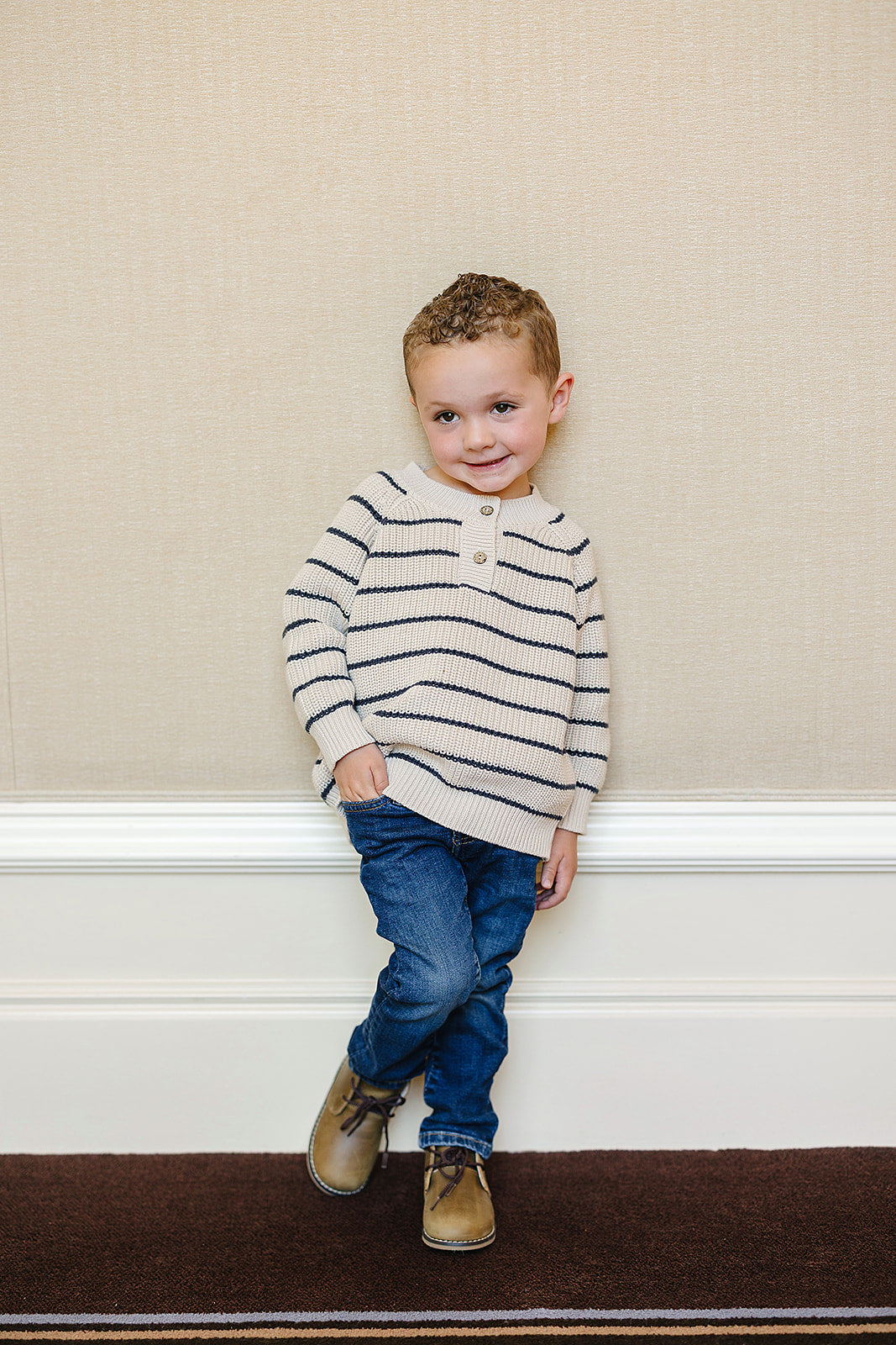 Young boy wearing a classic striped knit baby sweater, smiling with a playful pose against a neutral background.