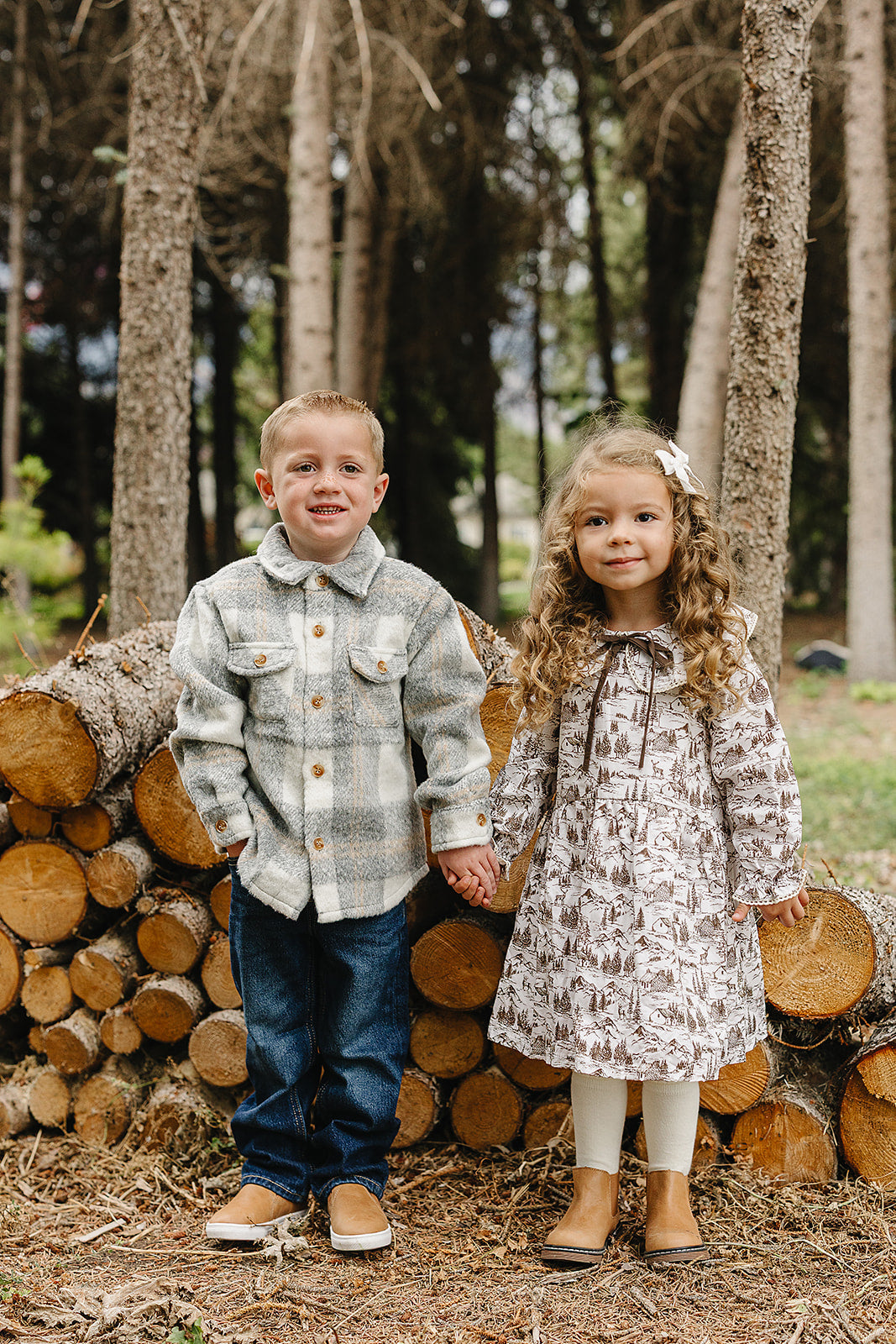 Two children holding hands outdoors, dressed in a grey plaid kids shacket and a cute patterned dress.