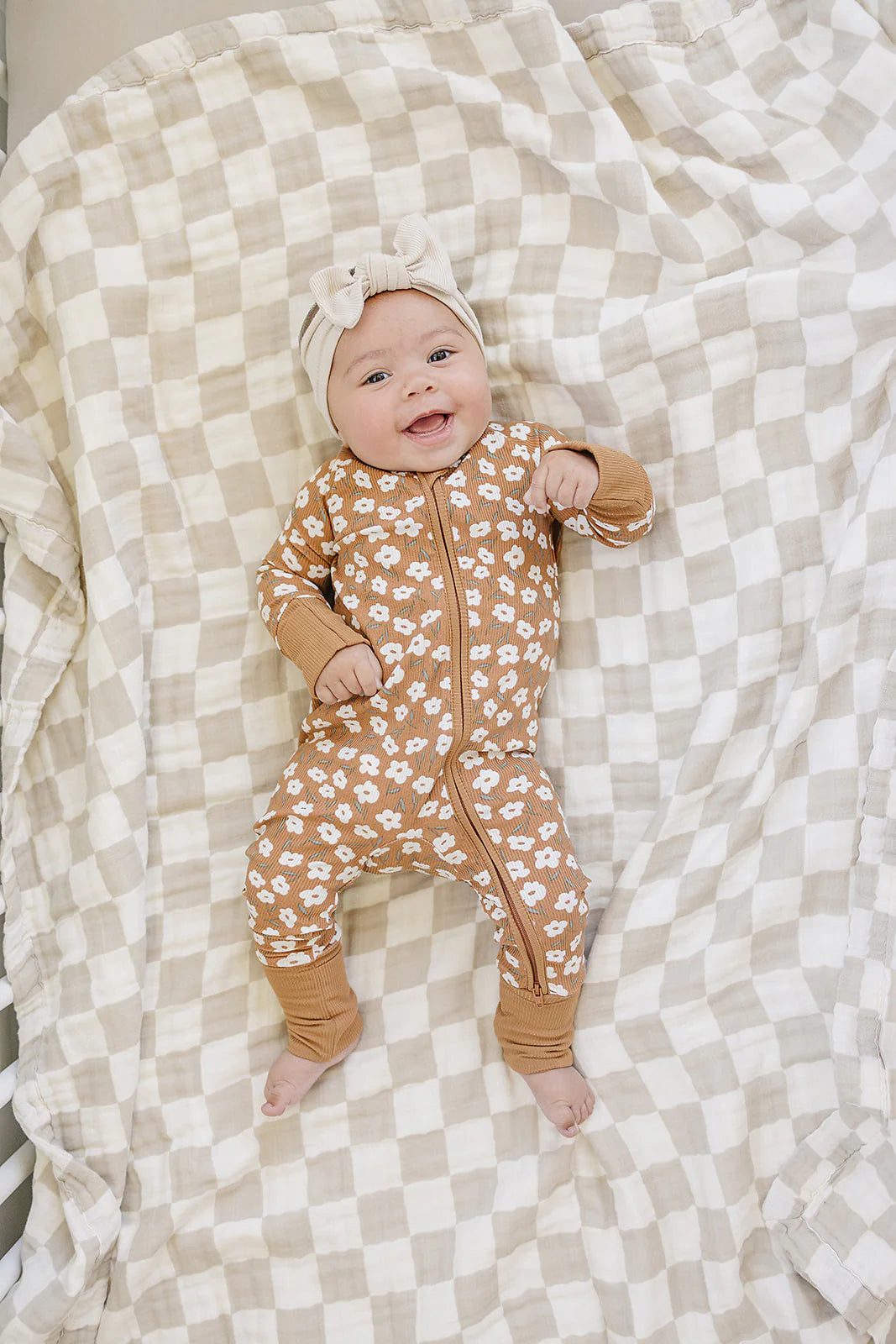 Baby in mustard floral ribbed bamboo zipper footie on a patterned blanket, smiling happily.