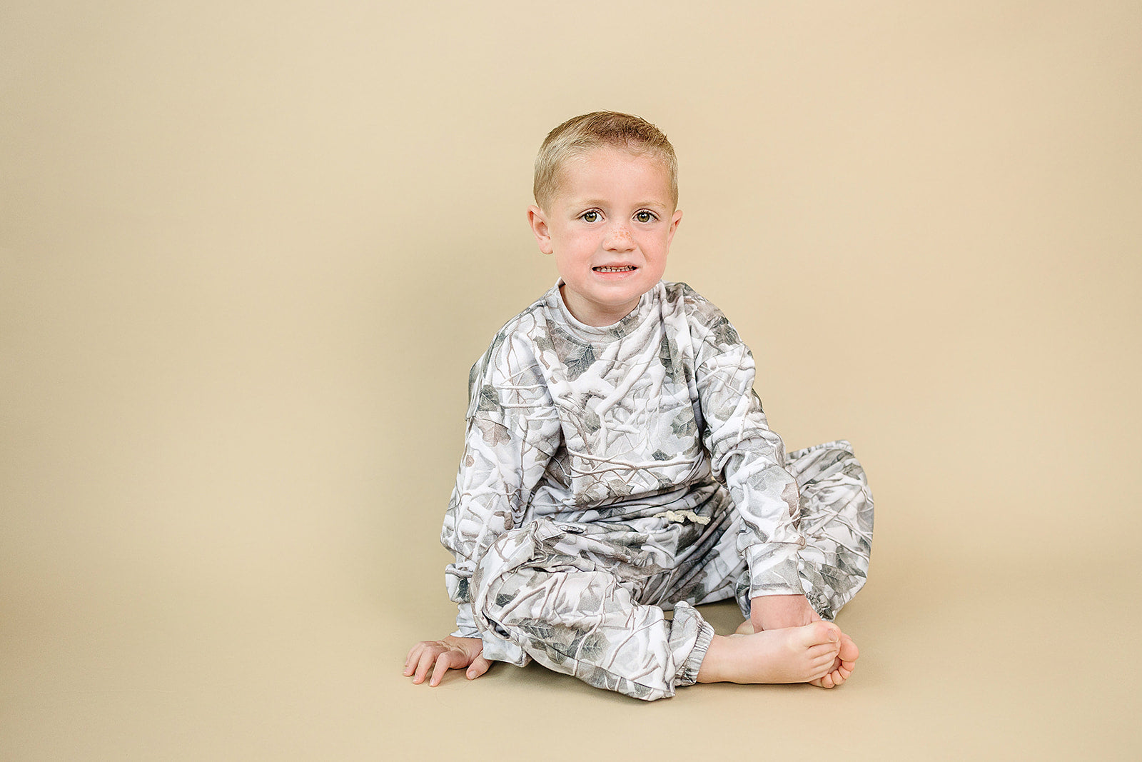 Camo kids lounge set featuring a young boy sitting in a camo print hoodie and matching cargo joggers.