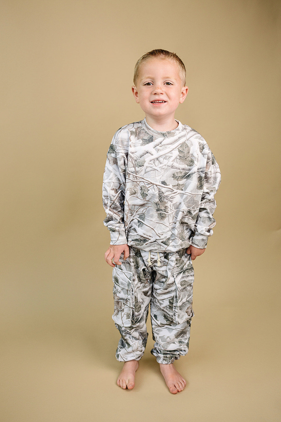 Camo kids lounge set featuring a young boy wearing a pullover hoodie and cargo joggers in a camo print.