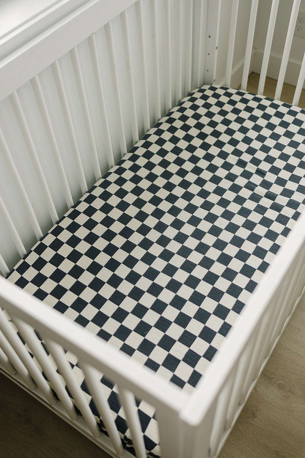 Muslin Crib Sheet - Charcoal Checkered in a white crib, showcasing its stylish checkered design.