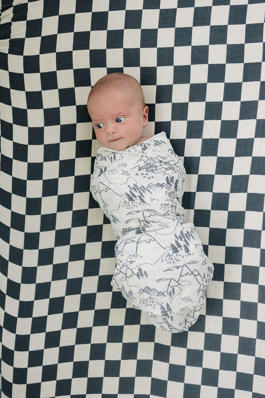 Muslin Crib Sheet with charcoal checkered pattern featuring a cozy swaddled baby.