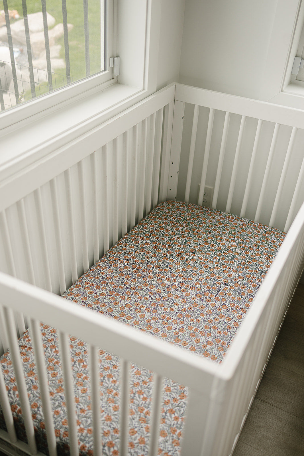 Bamboo crib sheet featuring a dainty meadow floral design in a white crib surrounded by natural light.