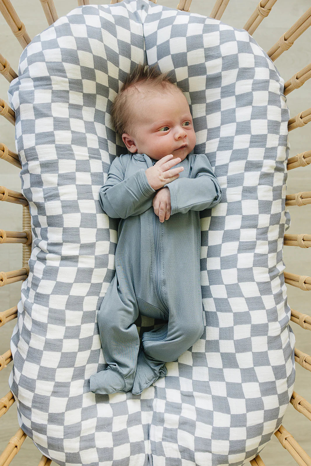 Baby lying in a cozy Bamboo Footed Zipper - Dusty Blue pajamas on a checkered blanket in a crib.