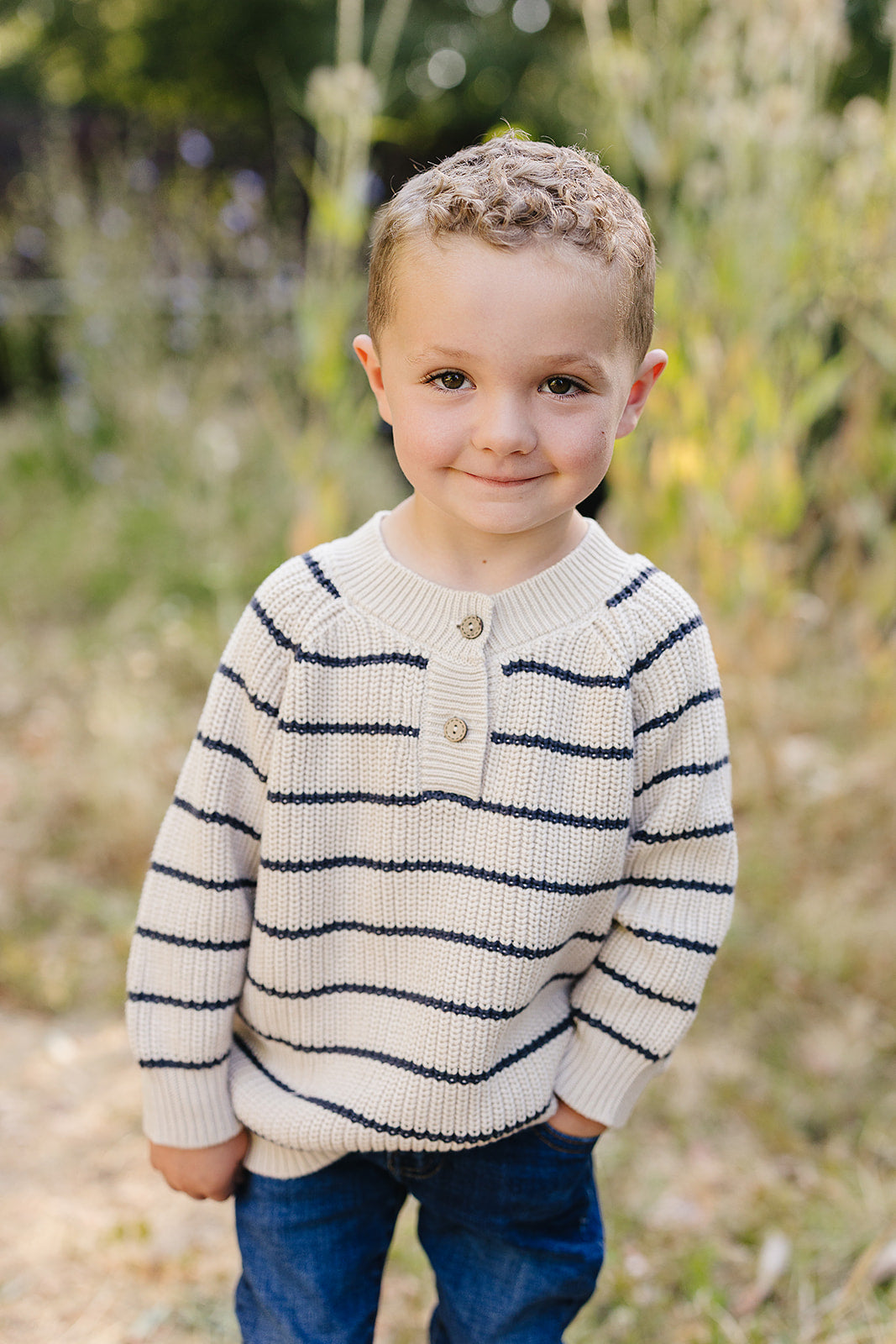 Smiling child wearing a classic striped knit sweater for babies & kids, featuring navy and cream stripes and a two-button henley neckline.