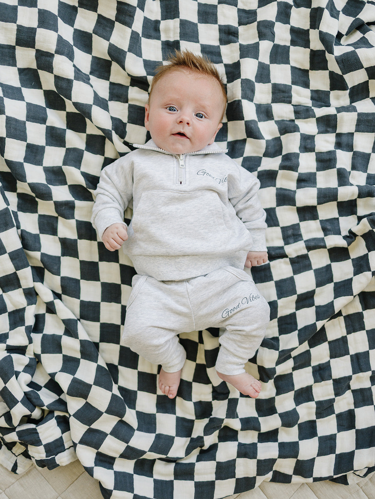 Adorable baby in a unisex French terry quarter zip set, lying on a checkered blanket, perfect for school outfits.