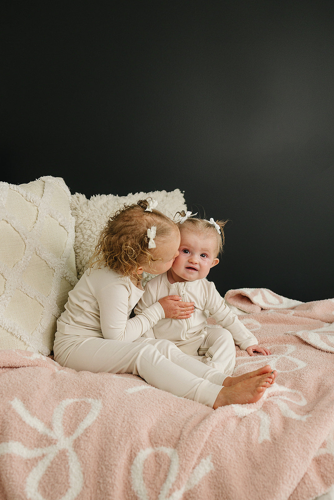 Two kids snuggling on a Pink Bow Plush Blanket, showcasing its softness and playful charm.