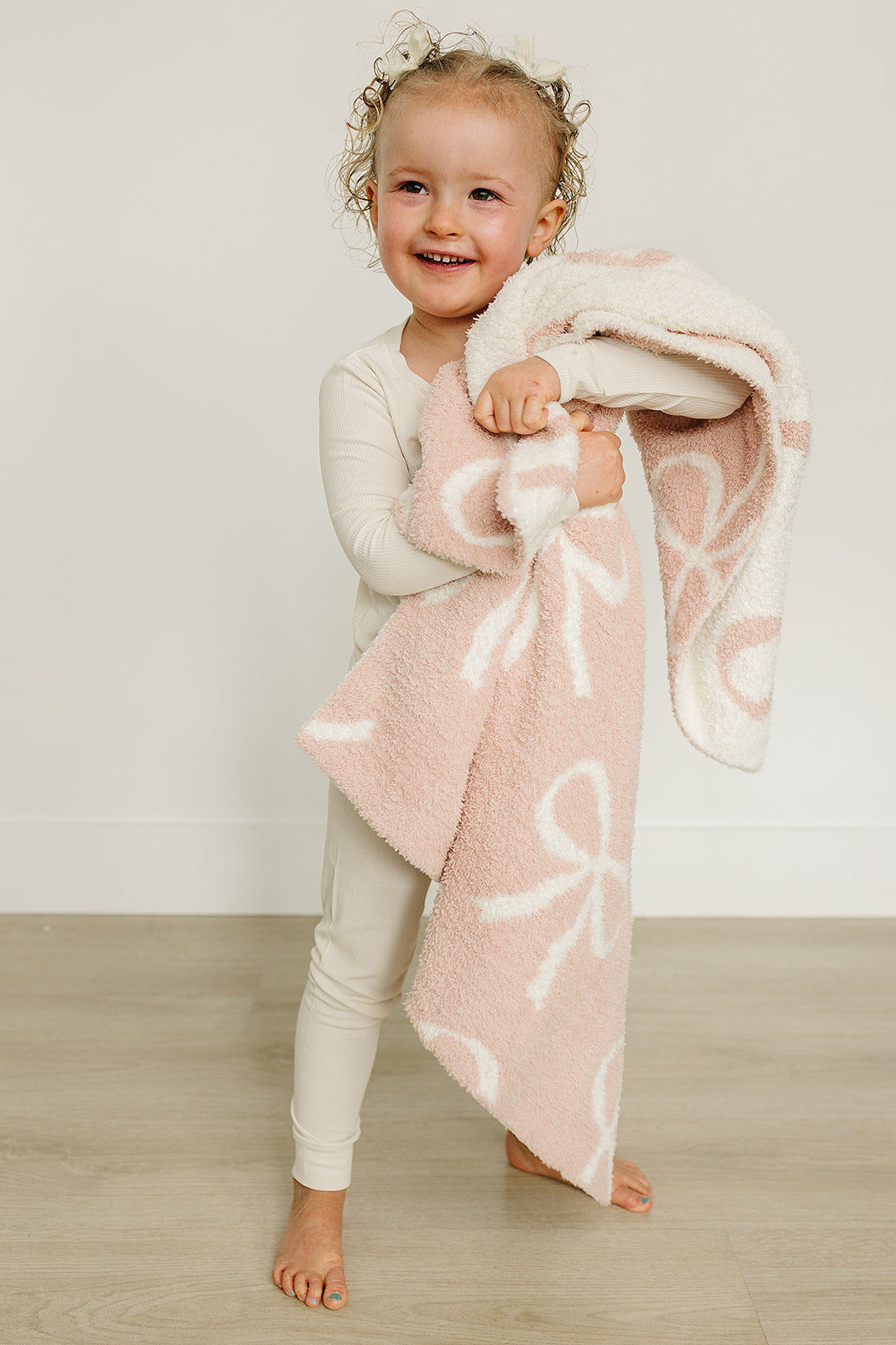 Child holding the Pink Bow Plush Blanket, showcasing its soft texture and playful design in a bright, cheerful setting.