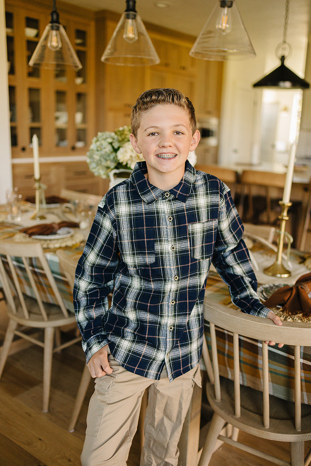 Boy wearing a navy plaid button-up shirt in a cozy dining room setting, showcasing a kids plaid shirt style.