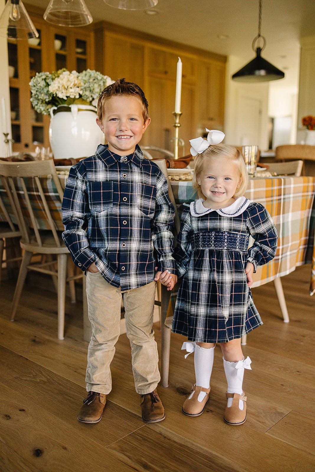 Two children in navy plaid outfits, showcasing a kids plaid shirt and a matching dress in a cozy indoor setting.