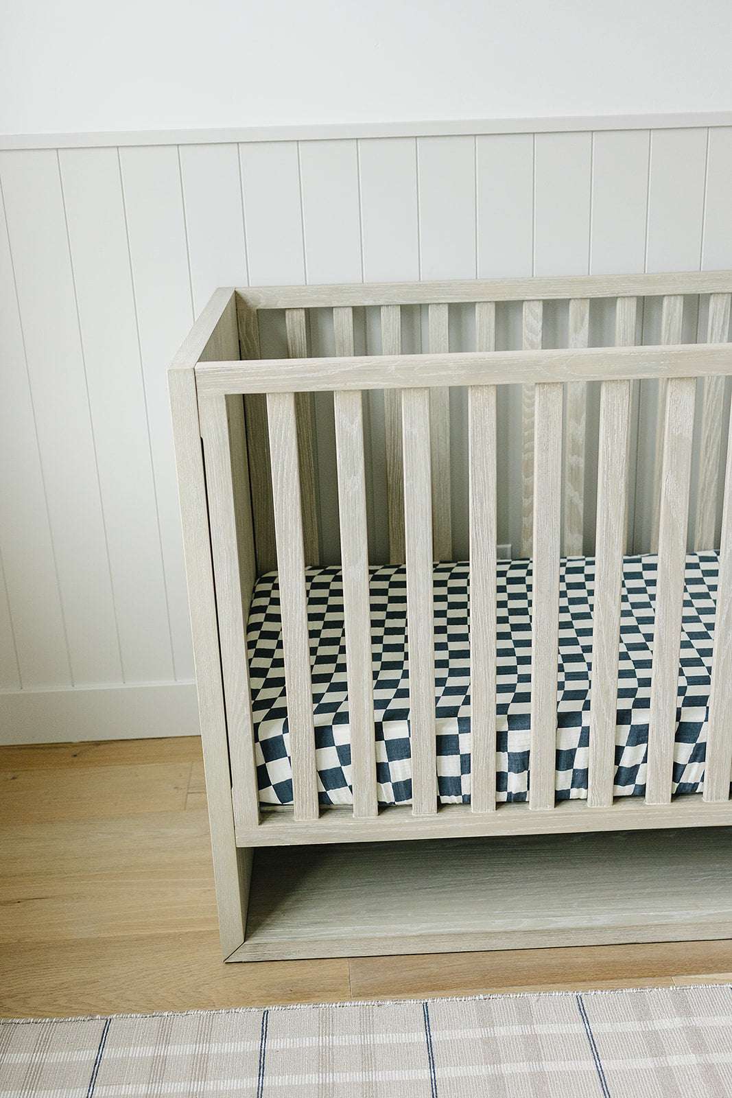 Muslin Crib Sheet - Charcoal Checkered fitted on a modern wooden crib in a bright nursery setting.