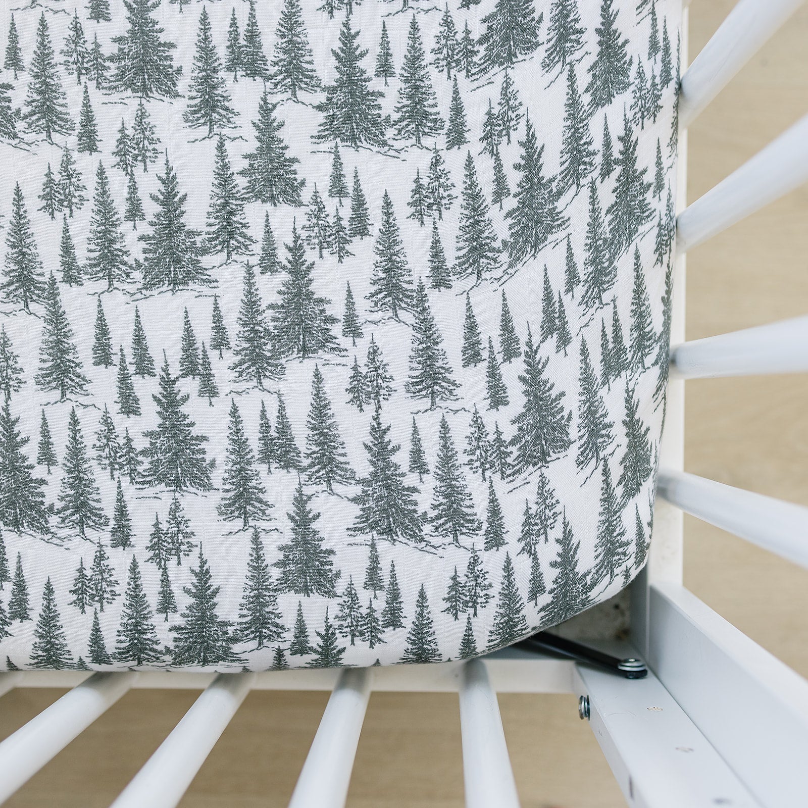 Muslin crib sheet featuring a forest woodlands design with trees in shades of green, perfect for a nursery.