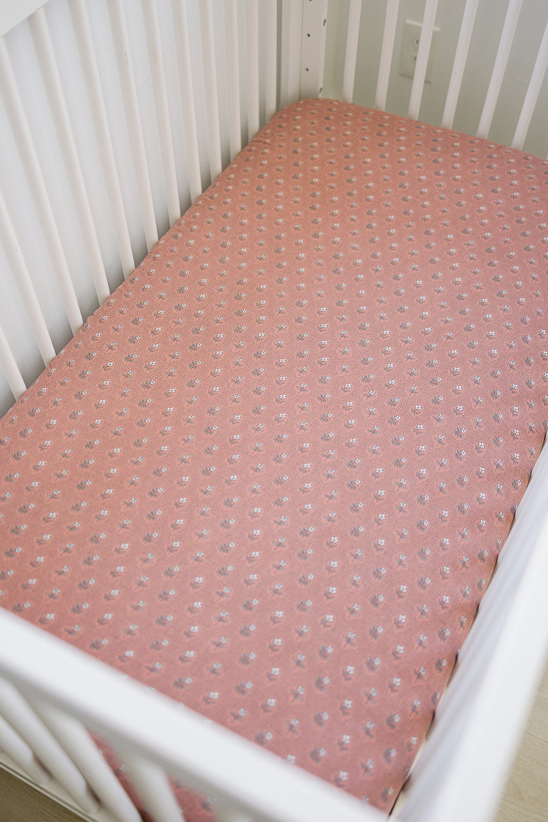 Muslin crib sheet in vintage pink floral design featured in a white crib, perfect for a cozy sleep environment.