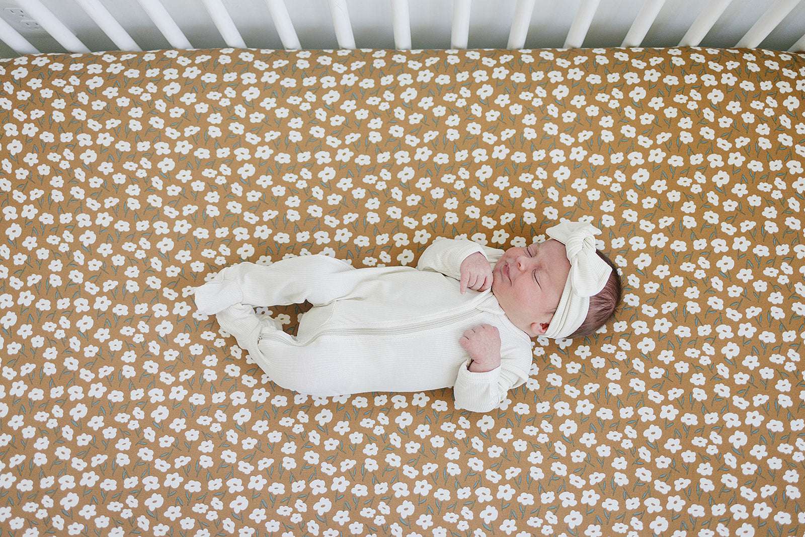Bamboo Stretch Crib Sheet with mustard floral print and a sleeping newborn in a crib.