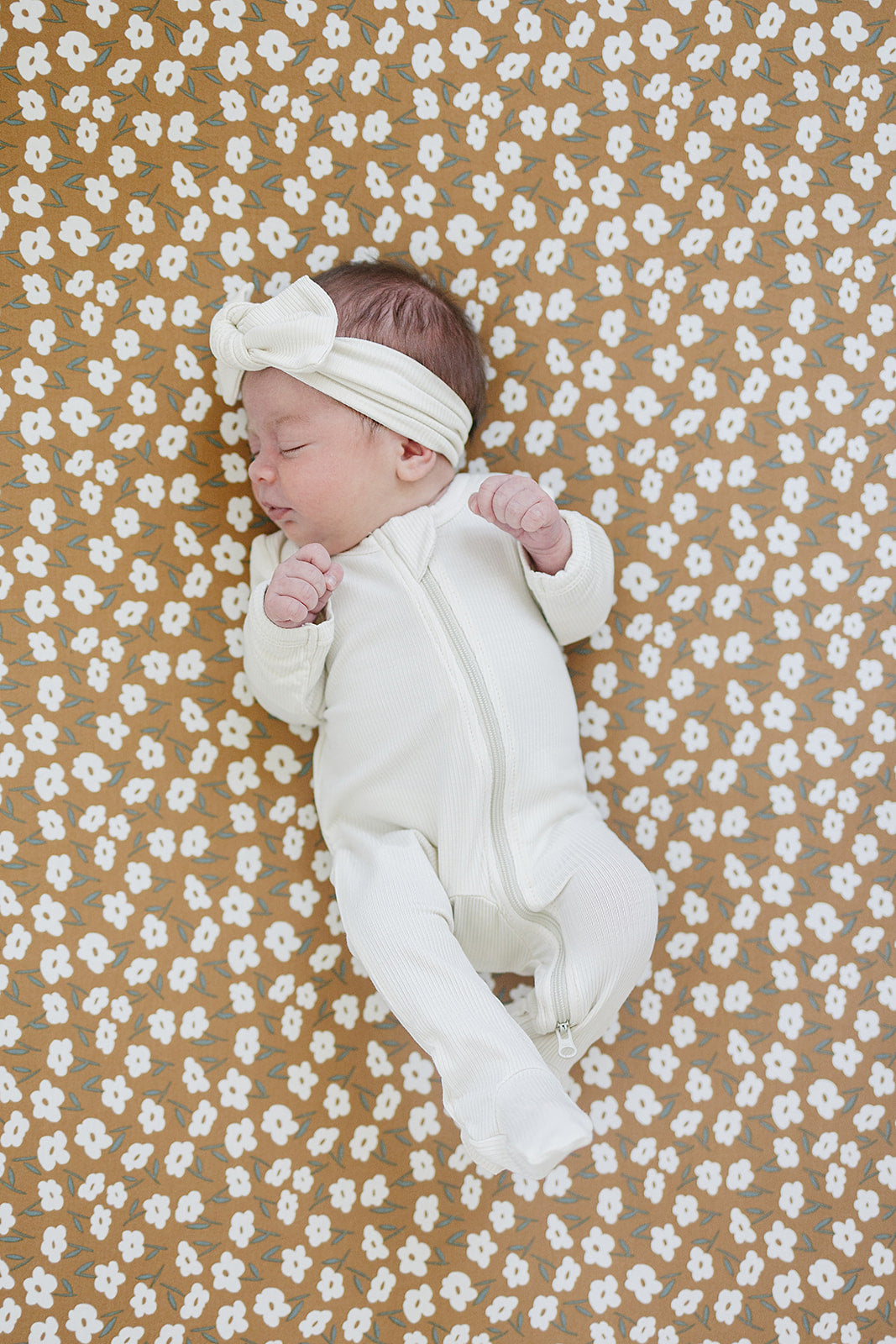 Cream ribbed bamboo zipper footie on baby, featuring soft fabric and cute headband, on a floral blanket.