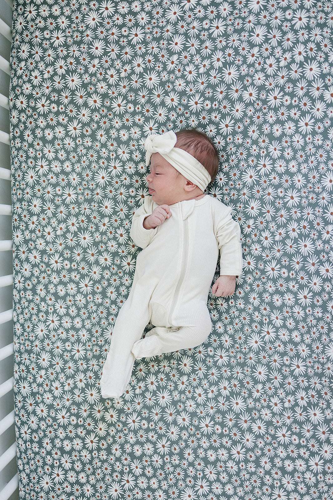 Newborn lying on Bamboo Stretch Crib Sheet with dark green daisy print, showcasing comfort and style in the nursery.