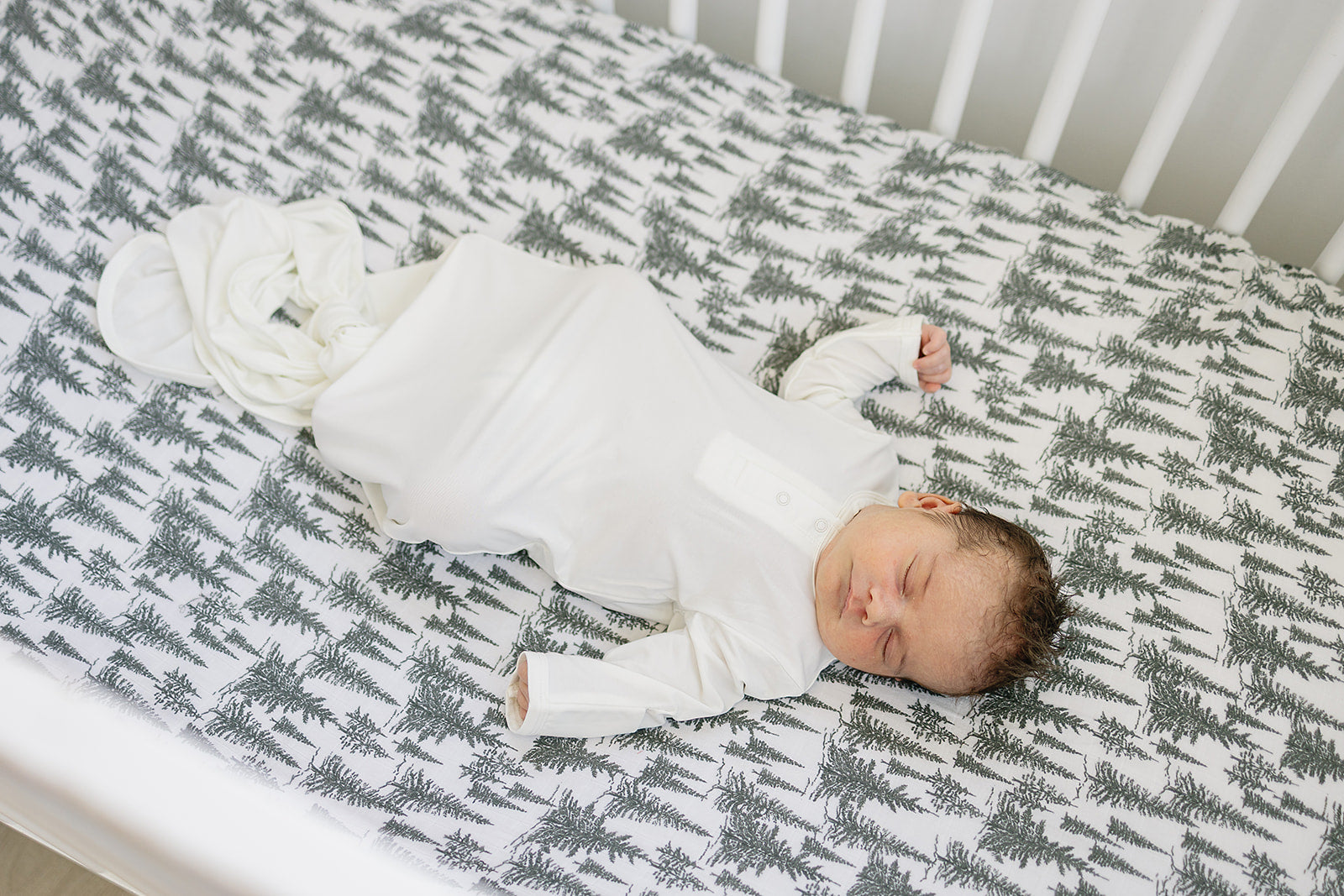 Muslin crib sheet in forest woodlands design with a sleeping baby on a crib mattress.