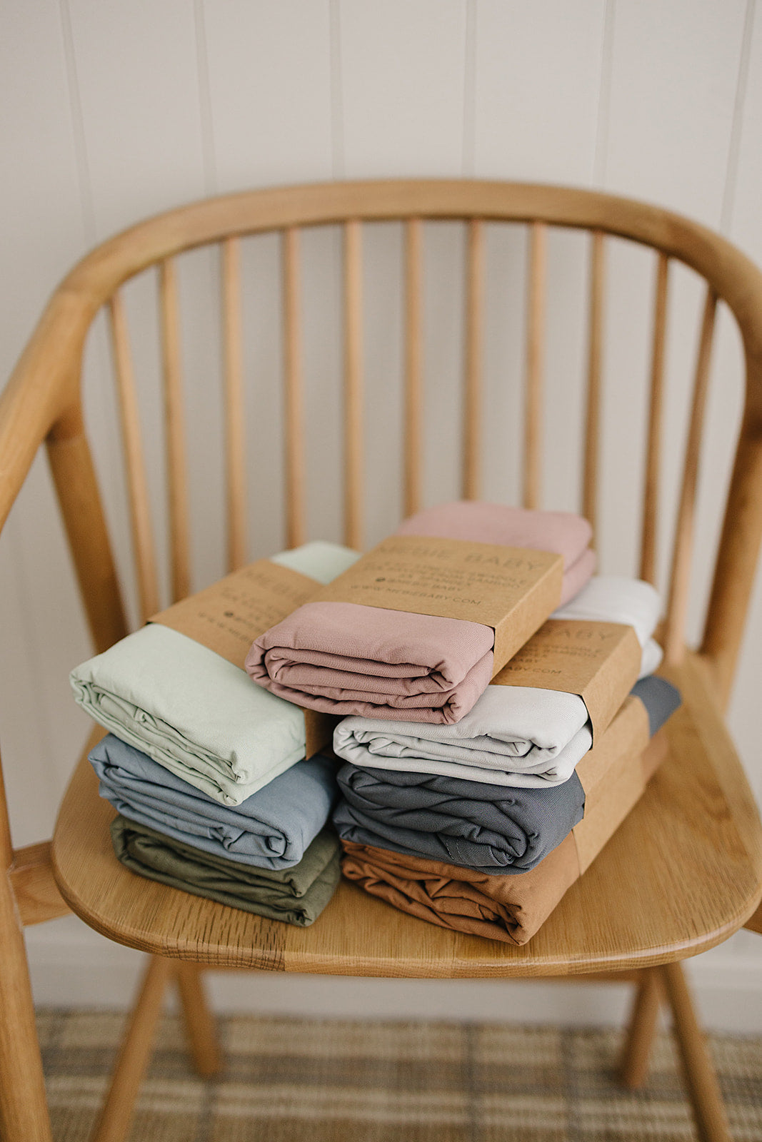 Bamboo Stretch Swaddle Sage and other colors neatly stacked on a wooden chair.