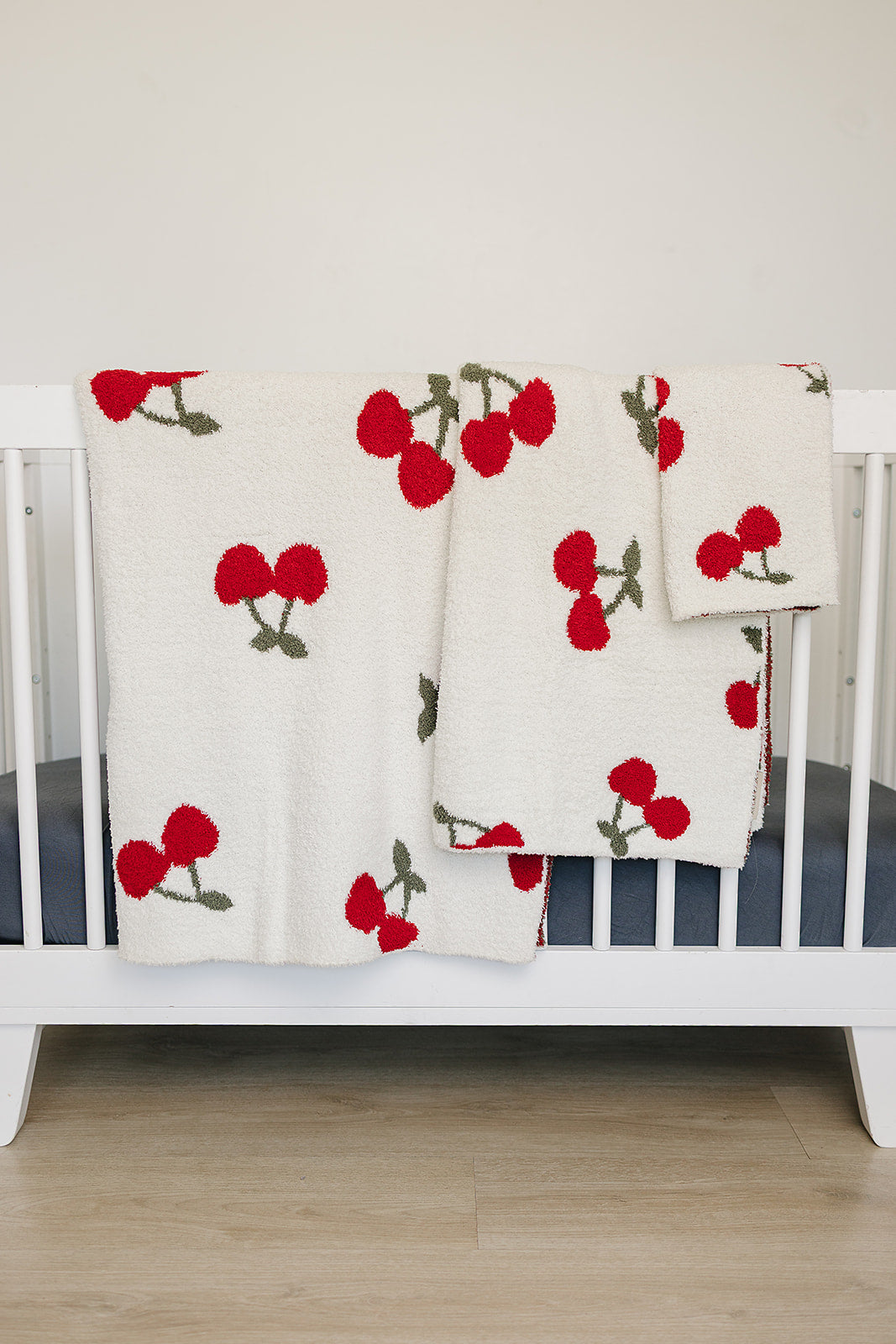 Baby plush blanket with a cherry print hanging over a crib in a stylish nursery setting.