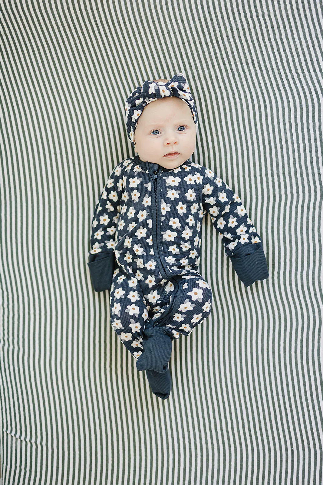 Navy daisy ribbed bamboo zipper footie on a baby with a matching headband, surrounded by a striped blanket.