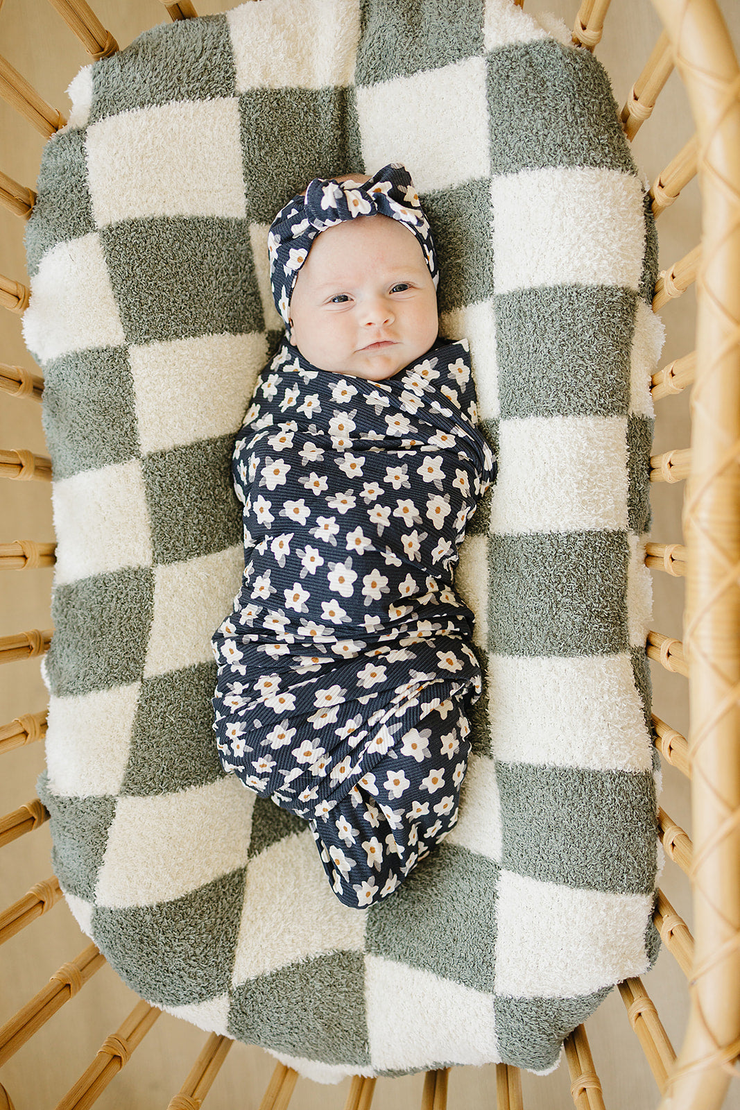 Baby wrapped in Bamboo Stretch Swaddle Navy Daisy Ribbed, resting on a cozy patterned blanket.
