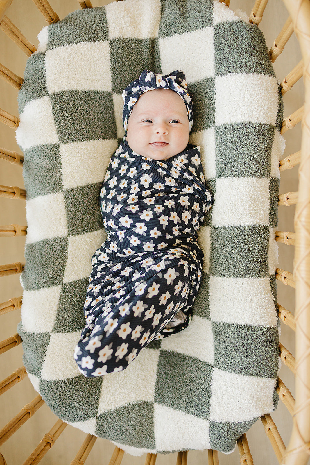 Baby wrapped in Bamboo Stretch Swaddle Navy Daisy Ribbed on a green and white checkered blanket.