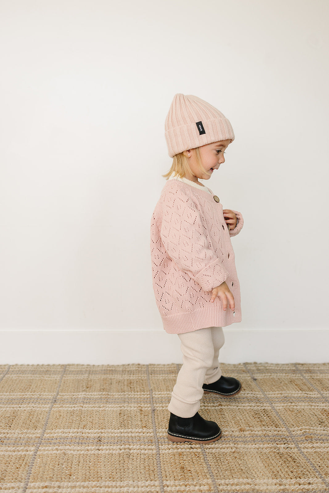 Baby Beanie in light pink worn by a toddler with a pink knitted cardigan and beige pants, adding warmth and style.