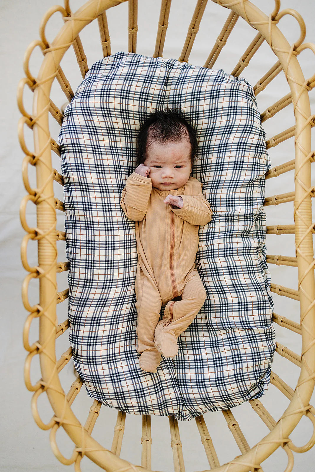 Baby wearing latte ribbed bamboo zipper footie in a cozy bassinet with plaid bedding.