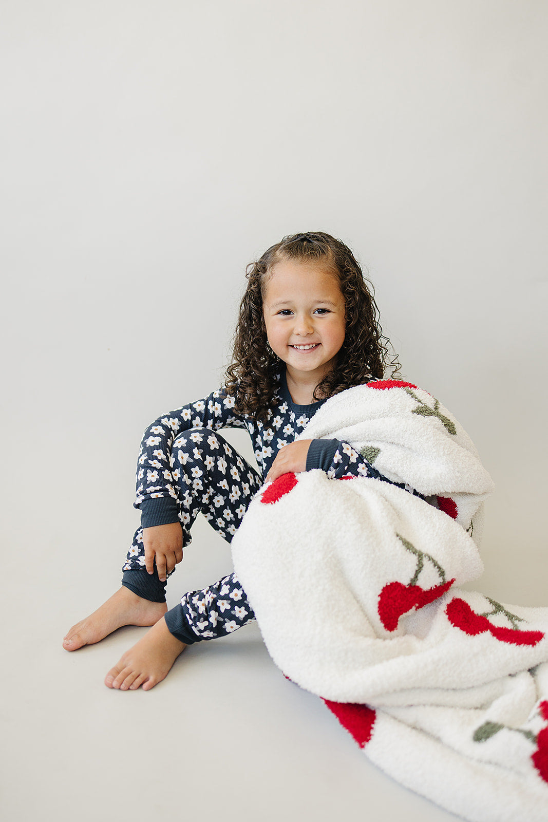 Child enjoying a cozy moment with a Cherry Baby Plush Blanket, featuring playful cherry print.