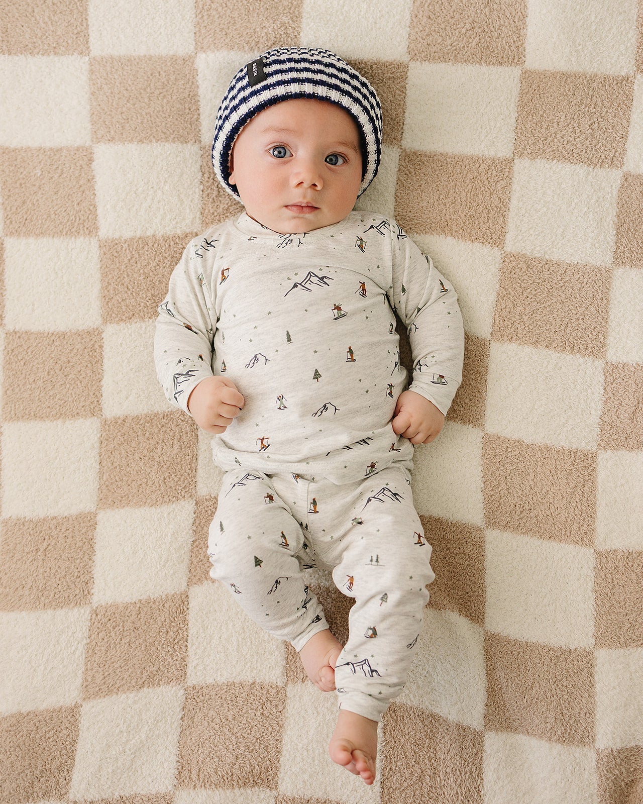 Baby wearing a chunky knit baby beanie in navy and white stripe, lying on a patterned blanket.