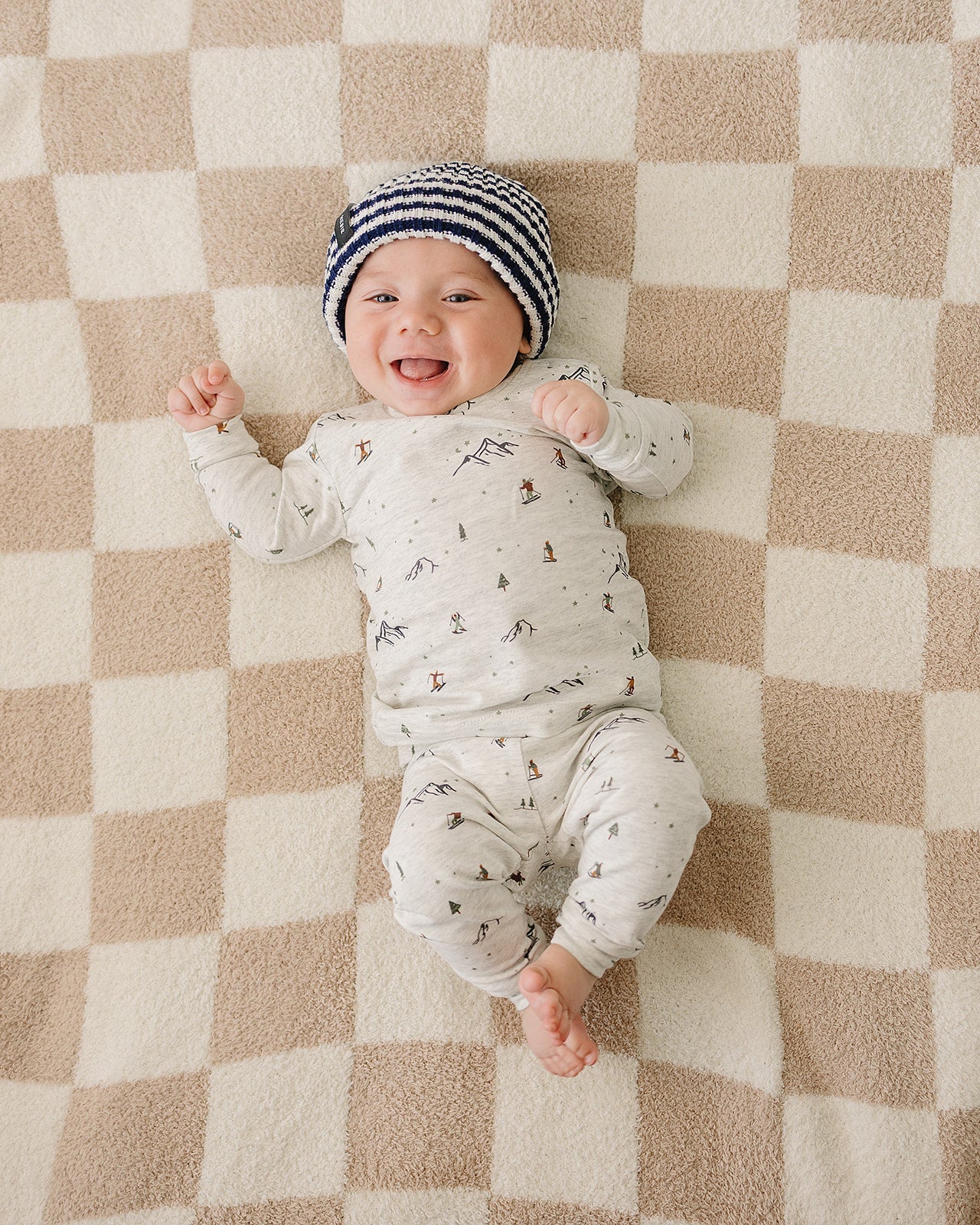 Smiling baby wearing a chunky knit baby beanie, laying on a blanket with checkered pattern.