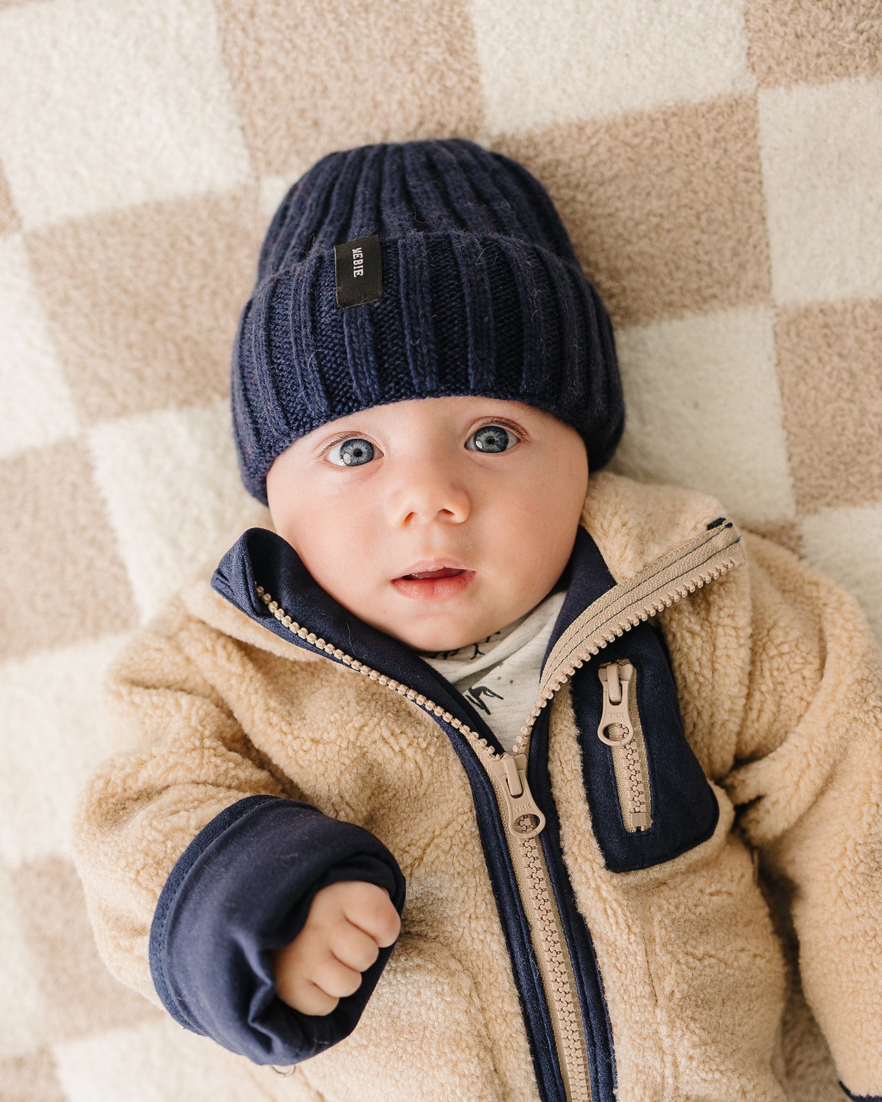 Cute baby wearing a chunky knit navy baby beanie, looking cozy and stylish on a soft blanket.