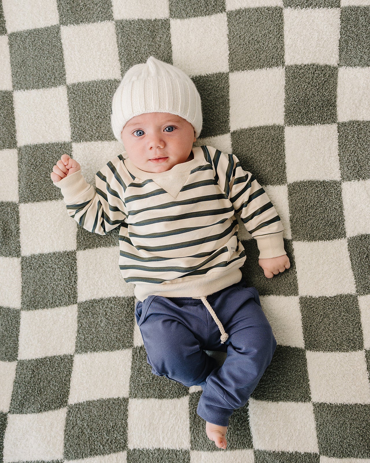Baby in striped shirt and navy pocket jogger pants for babies & kids, lounging on a checkered blanket.