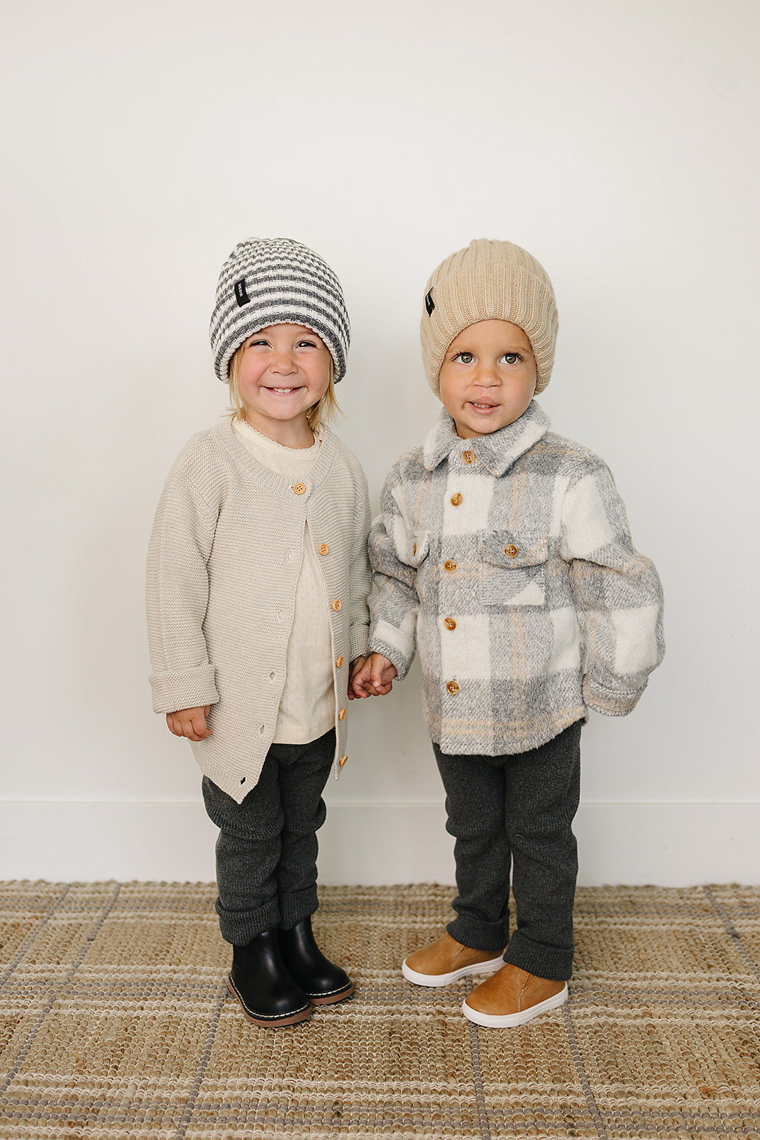 Two kids wearing winter outfits, one in a grey plaid kids shacket and the other in a cream cardigan.