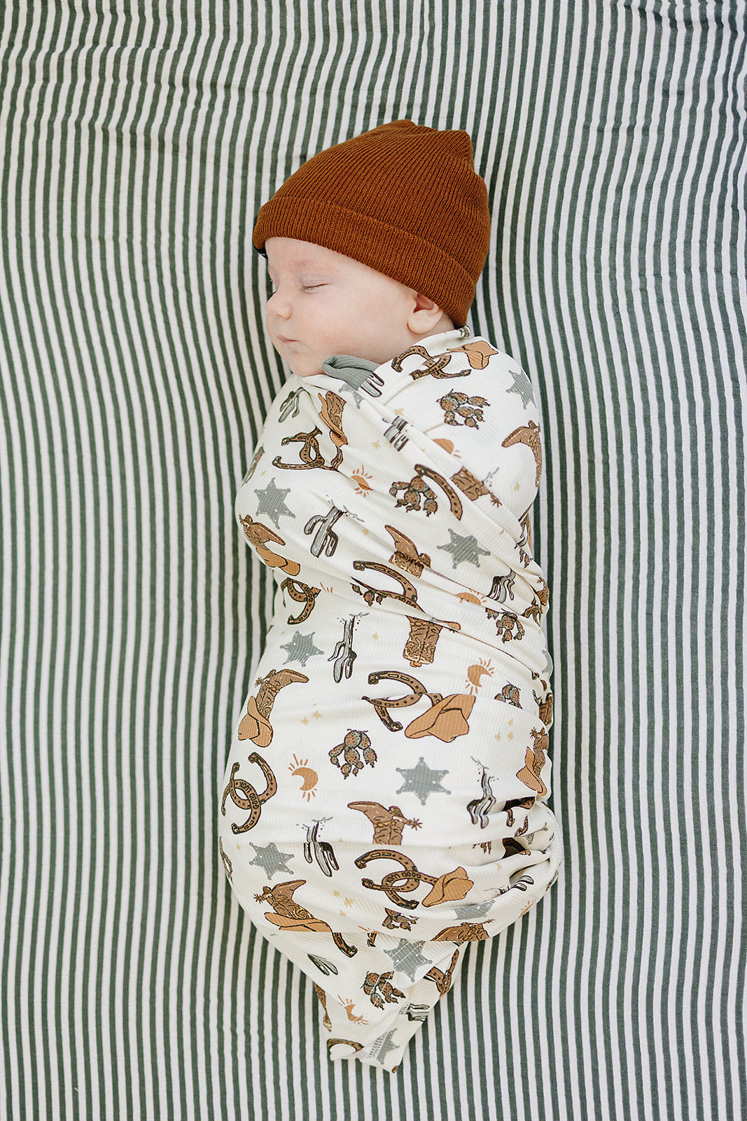 Baby wrapped in the Bamboo Stretch Swaddle Outlaw Cowboy Ribbed, featuring playful designs and a cozy hat.