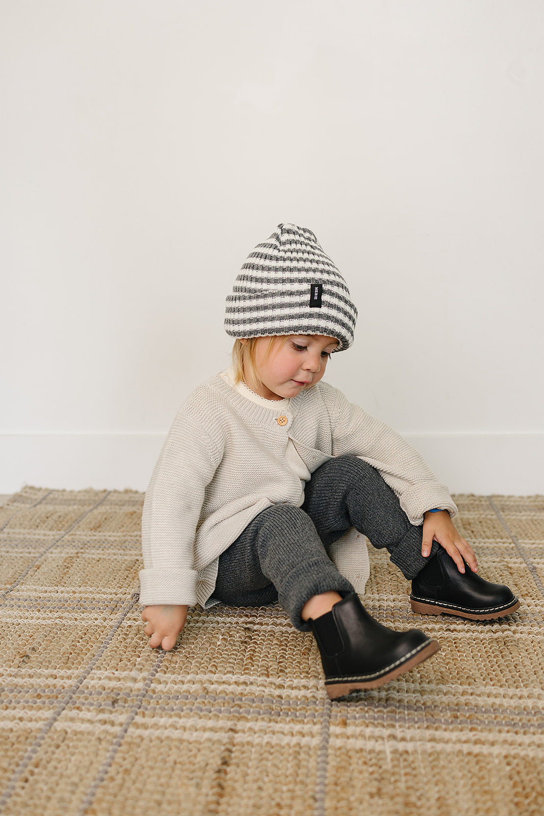 Baby wearing a chunky knit grey and white baby beanie, sitting on a rug, styled in cozy fashion.