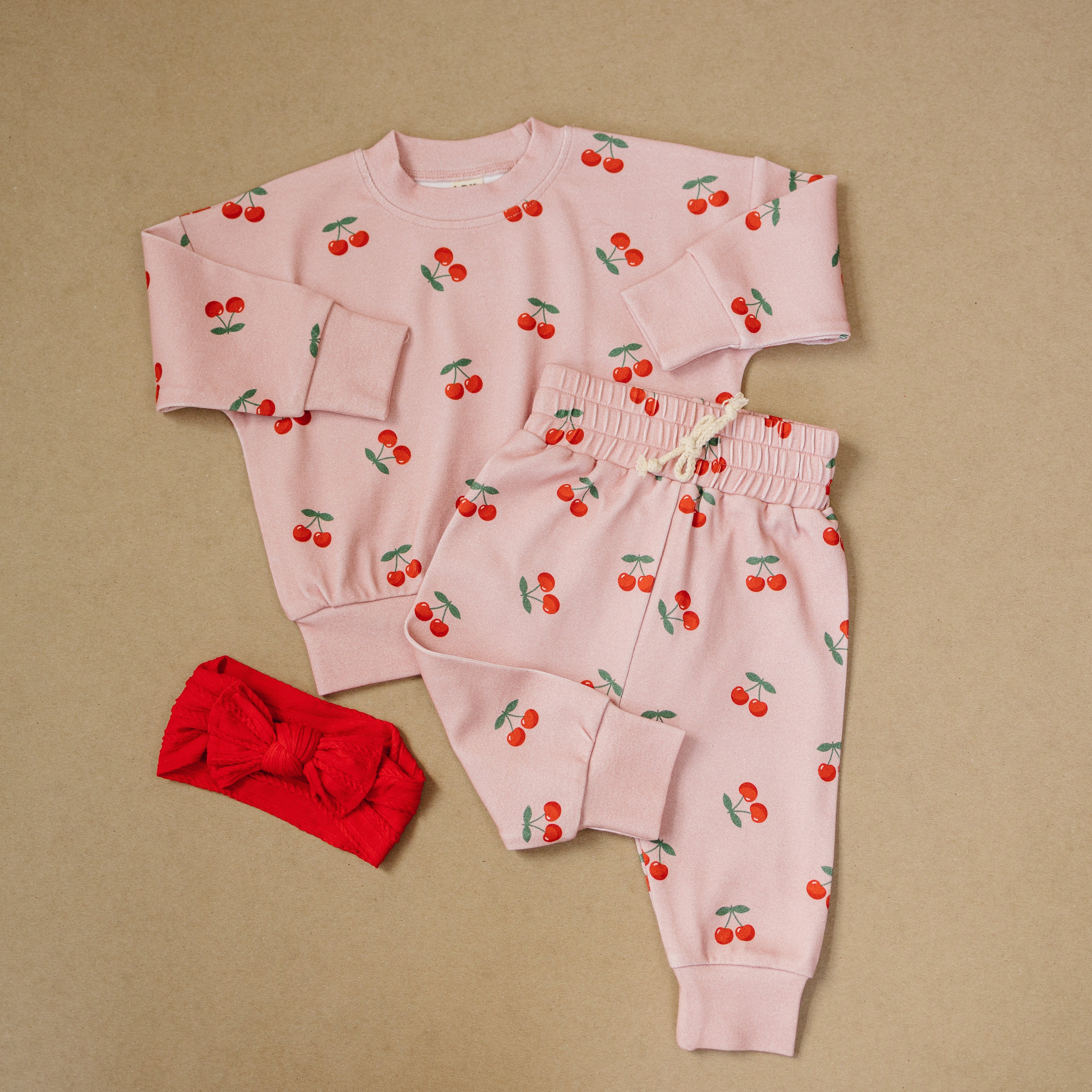 Blush Cherry Kids Lounge Set with cherry print top and jogger-style bottoms, plus a red hair accessory.