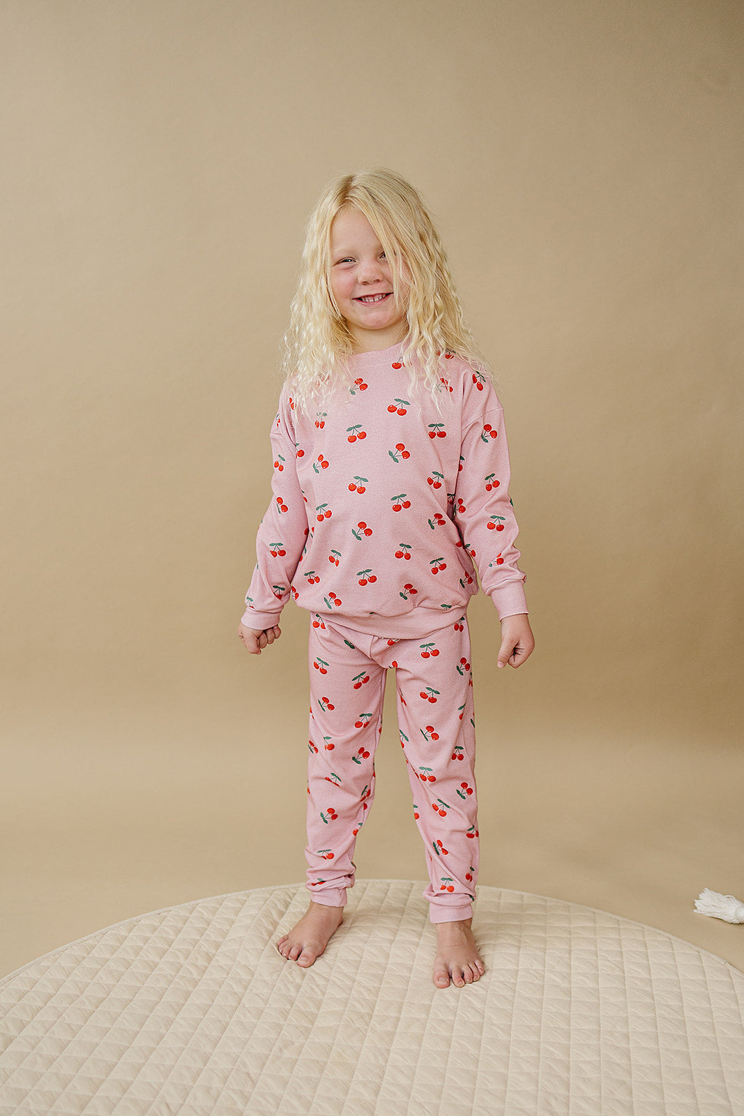 Blush Cherry Kids Lounge Set worn by a smiling girl on a beige background, showcasing a soft pink outfit with cherry prints.