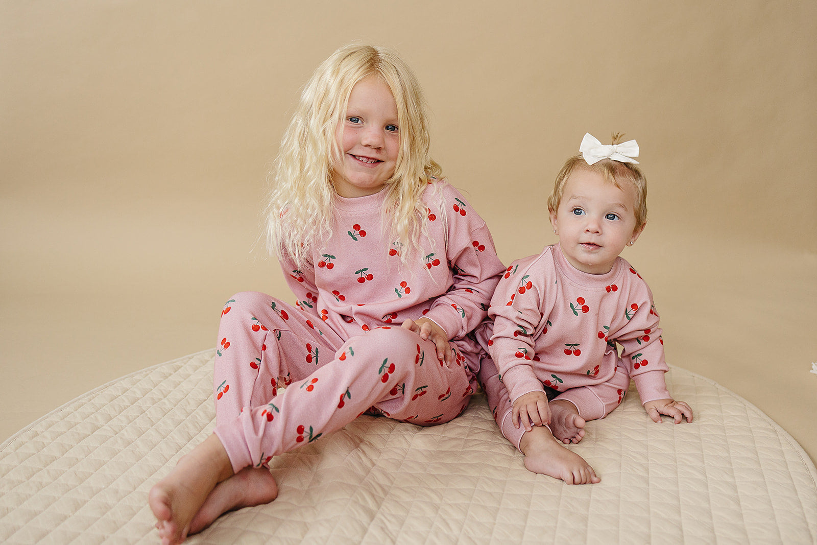 Blush Cherry Kids Lounge Set worn by a toddler and baby girl, featuring a playful cherry print in soft blush hue.