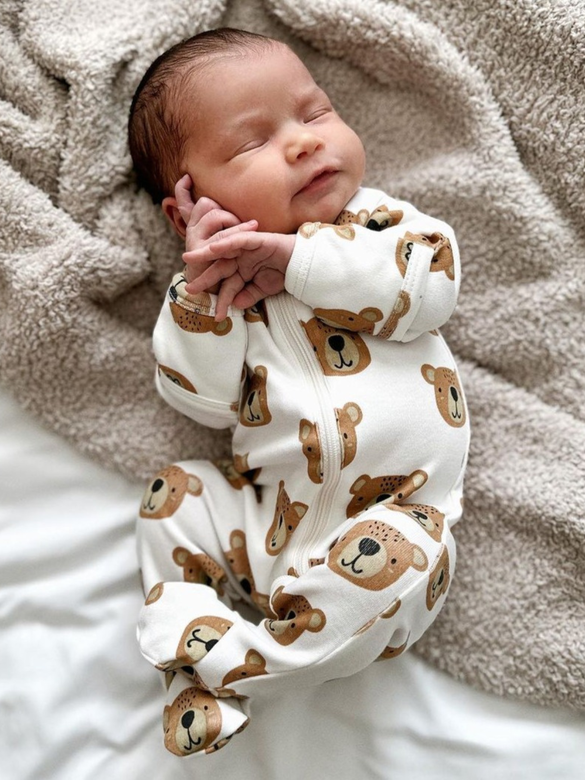 Infant sleeping in Baby Bear organic zip footie with bear print, cozy on a soft blanket for sweet dreams.