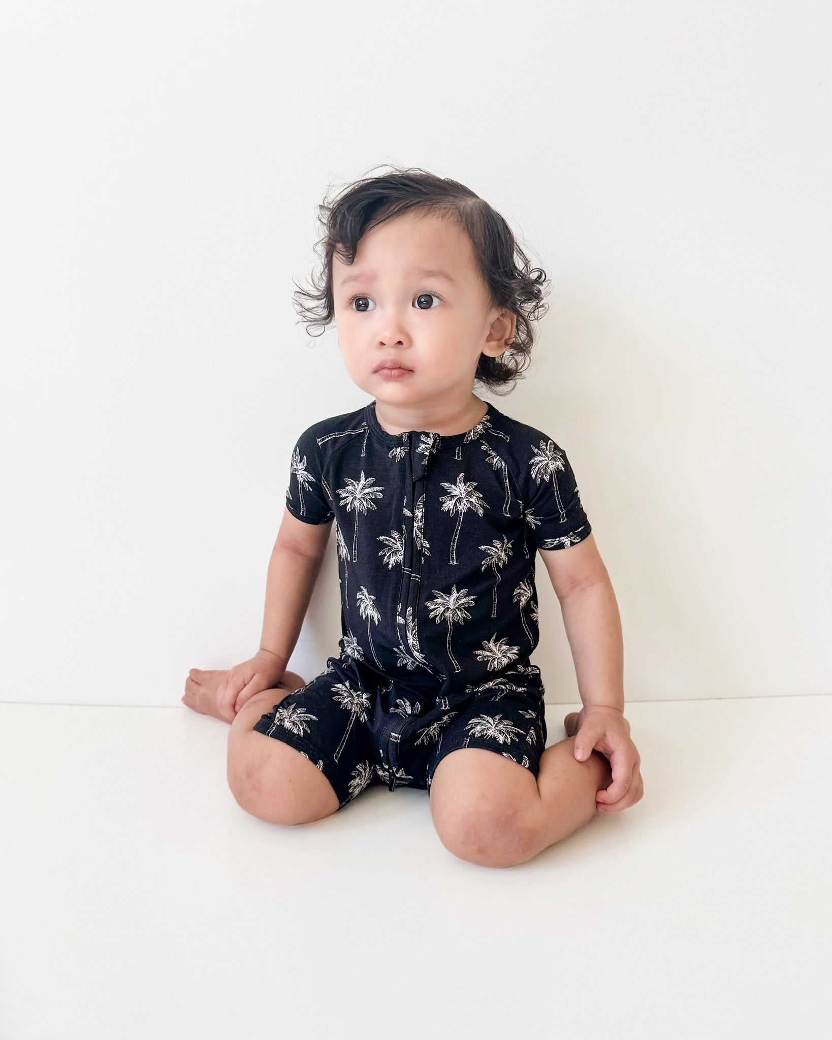Baby in black bamboo romper with palm print, perfect for sunny adventures and warm weather play.